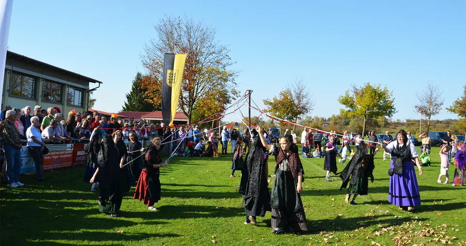 Tanzpaare in Tracht tanzen auf dem Festplatz, ringsum viele Zuschauerinnen und Zuschauer unter blauem Herbsthimmel